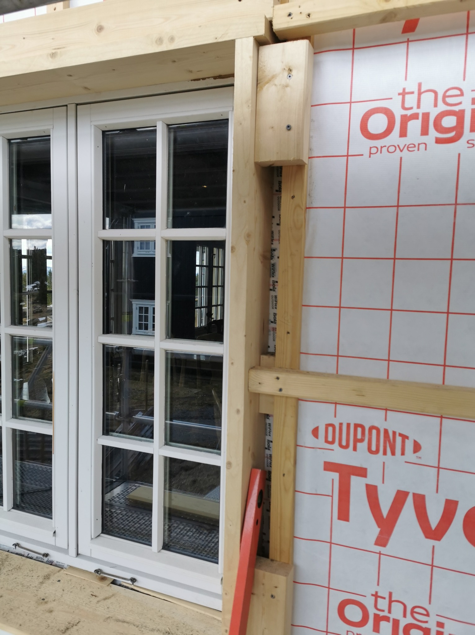 Montaż stolarki okiennej w domu szkieletowym z widocznym poziomowaniem i membraną izolacyjną DuPont Tyvek.