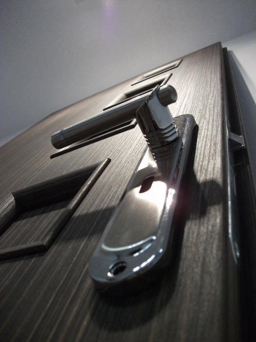 Nowoczesne drzwi wejściowe z ciemnego drewna z chromowaną klamką, widok z dołu pod kątem.