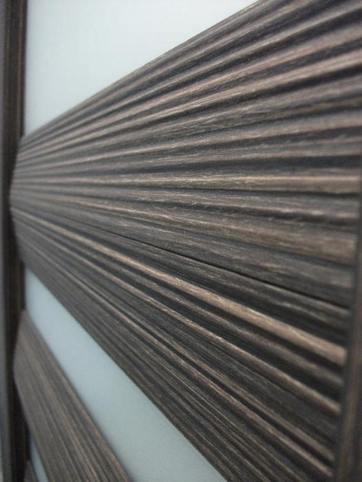 Fragment nowoczesnych drzwi z poziomymi, żłobionymi lamelami w odcieniach brązu i szarości, widoczne pod kątem.