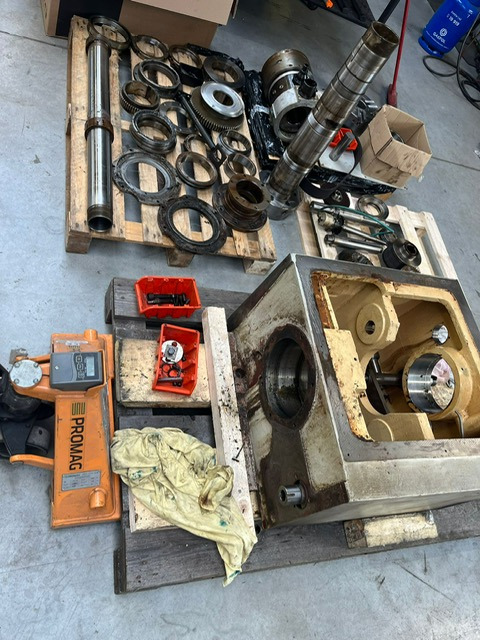 Elementy tokarki CNC, w tym wrzeciono, przekładnie i obudowa, rozłożone na paletach podczas serwisu lub naprawy.