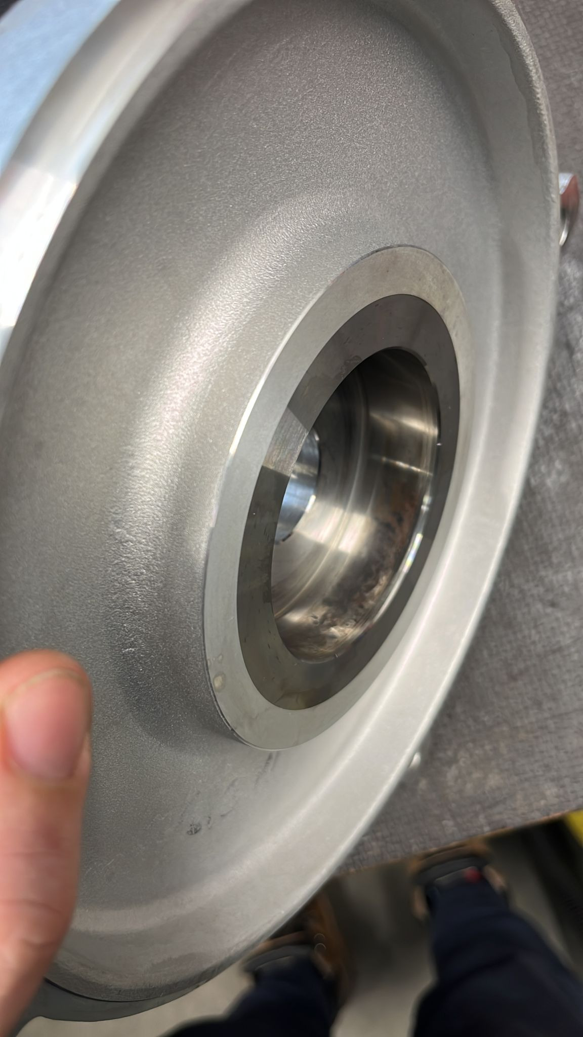 Szlifowany element metalowy z otworem centralnym, prawdopodobnie po obróbce CNC, widoczne ślady obróbki i odcisk palca.