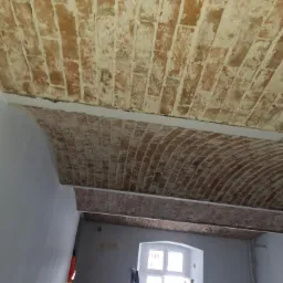 Ceglany łuk sufitowy po oczyszczeniu, widoczny fragment klatki schodowej i okno w tle.