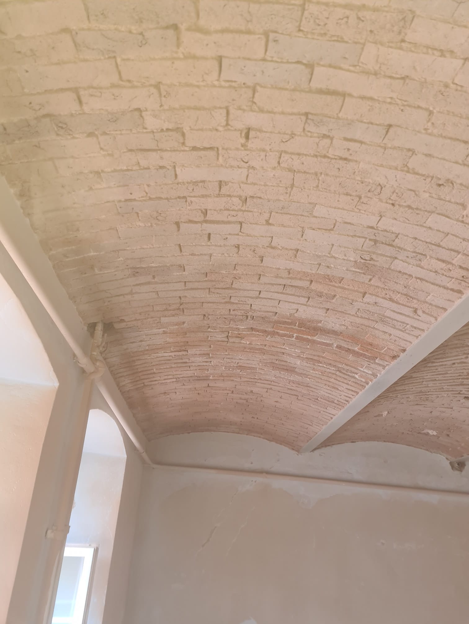 Malowany na jasny kolor ceglany łuk sufitowy w trakcie remontu, widoczne ślady szpachlowania na ścianach.