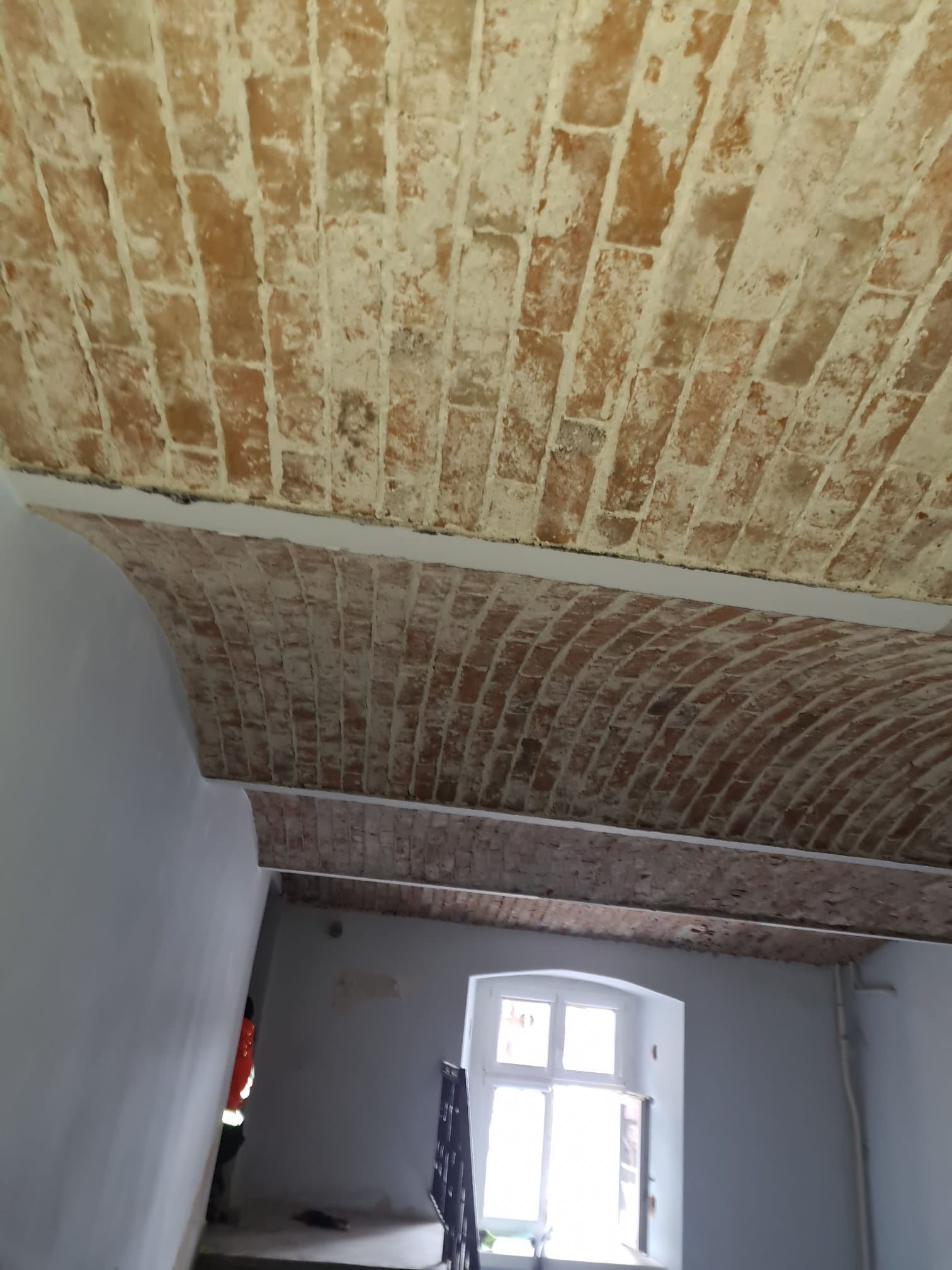 Ceglany łuk sufitowy po oczyszczeniu, widoczny fragment klatki schodowej i okno w tle.