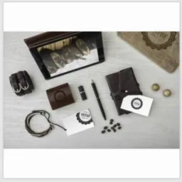 Kompozycja na jasnym drewnianym blacie: skórzane akcesoria, notes, długopis, pendrive, wizytówki z logo w stylu vintage, kulki i zdjęcie psa w ramce.