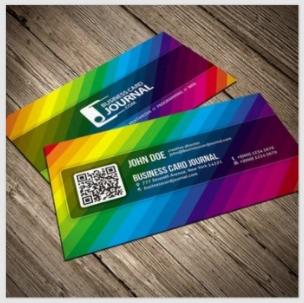 Dwie wizytówki ułożone na drewnianym stole. Wizytówki mają tęczowe, ukośne paski i zawierają logo, kod QR oraz dane kontaktowe.