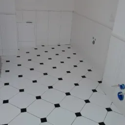 Wykończona łazienka z białymi płytkami ściennymi i podłogą w biało-czarną szachownicę, widoczne przyłącza hydrauliczne i zabudowa geberit.