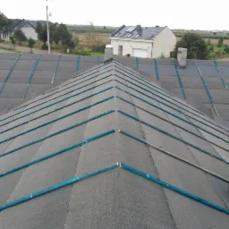 Przygotowanie dachu pod krycie, widoczna membrana dachowa i listwy kontrłat, fragment komina w tle.