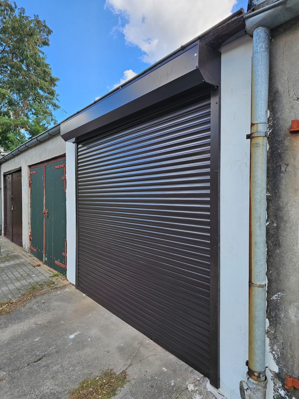 Zamknięta, brązowa osłona na garażu z widoczną rynną i starą nawierzchnią podjazdu.