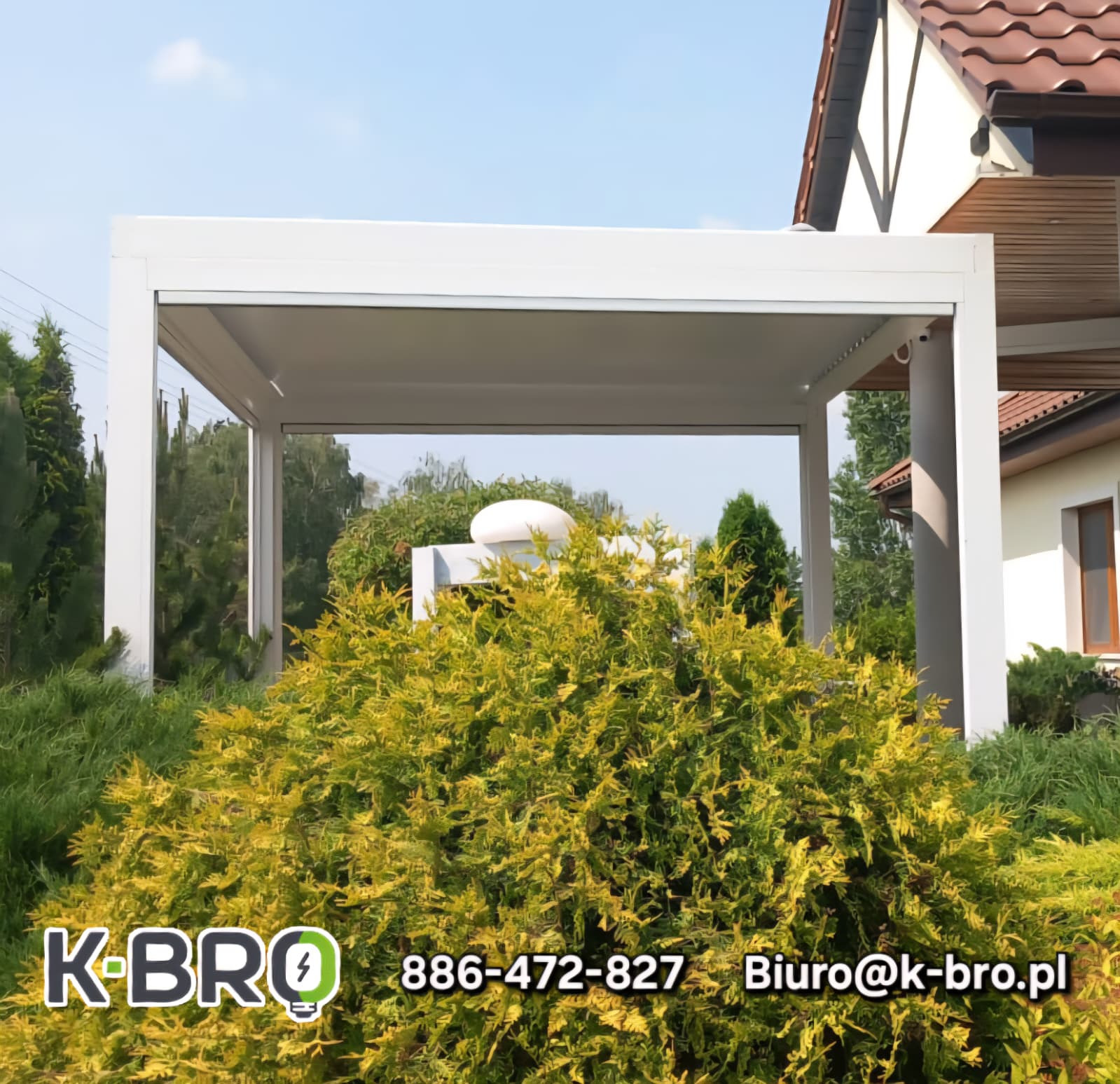 Nowoczesna, biała pergola tarasowa z płaskim dachem, widoczna zza krzewu. W tle dom z brązowym dachem. Słoneczny dzień.