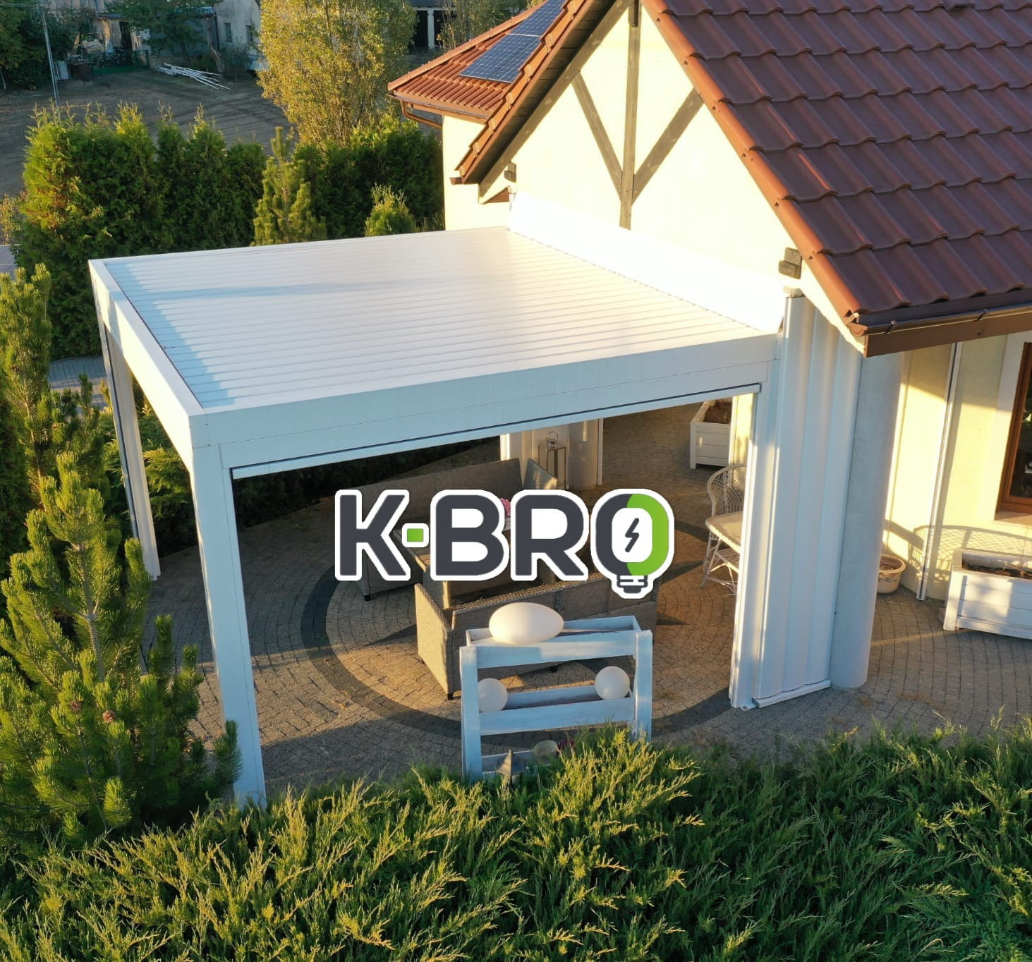 Nowoczesna, biała pergola tarasowa z lamelami, widok z góry, otoczona zielenią. Elementy dekoracyjne na tarasie. Dach z paneli.