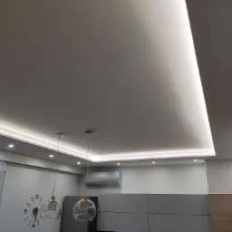 Nowoczesny sufit podwieszany z oświetleniem LED, widoczne lampy wiszące z przezroczystymi kloszami i zegar ścienny z rzymskimi cyframi.