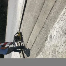 Pracownik ubija podłoże pod drogę zagęszczarką wibracyjną, widoczne świeże ślady po ubijaniu i tymczasowe oznakowanie.