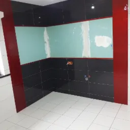 Łazienka w trakcie remontu: czarne i białe płytki, czerwone akcenty, ściana przygotowana pod gładzie, widoczne instalacje hydrauliczne i elektryczne.