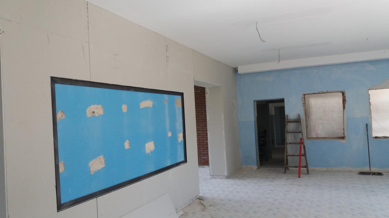 Wnętrze w trakcie remontu w Żywcu: ściany z płyt kartonowo-gipsowych, przygotowane otwory okienne i fragment niebieskiej ściany z łatami, widoczna drabina i podłoga z płytek.