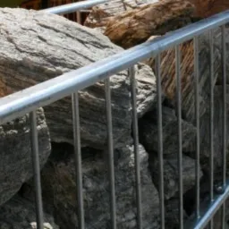 Gabionowa ściana z szarego kamienia w metalowej siatce o regularnych oczkach, widoczna z bliska.