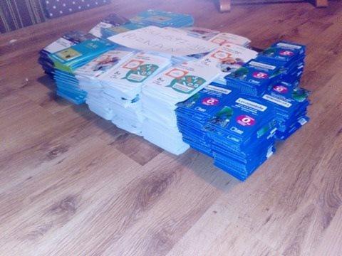 Stosy opakowań na podłodze z laminatu, różne kolory i wzory, częściowo zasłonięte kartką z napisem 'HUZNAM'