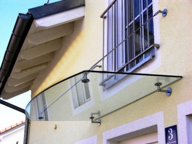 Szklany daszek nad wejściem do budynku, zamocowany na metalowych wspornikach, z widocznym numerem 3 na ścianie obok drzwi.