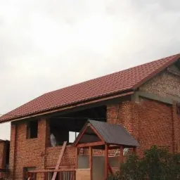 Ceglany budynek w trakcie wymiany dachu z widoczną konstrukcją więźby i czerwonym pokryciem.