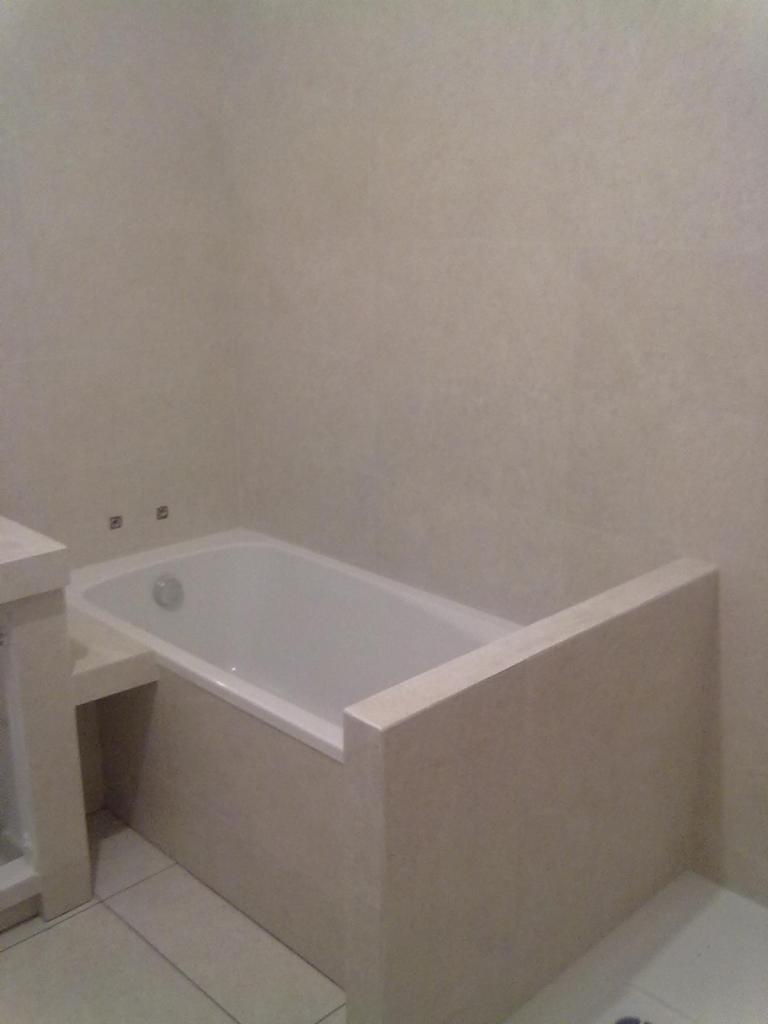 Wykończona łazienka z białą wanną obudowaną jasnobeżowymi płytkami ceramicznymi, widok na narożnik wanny i fragment ściany z płytkami w tym samym odcieniu.