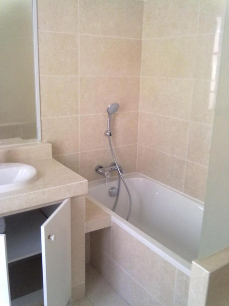 Wykończona łazienka z beżowymi płytkami, białą wanną i umywalką z szafką, widoczny zestaw prysznicowy i bateria.