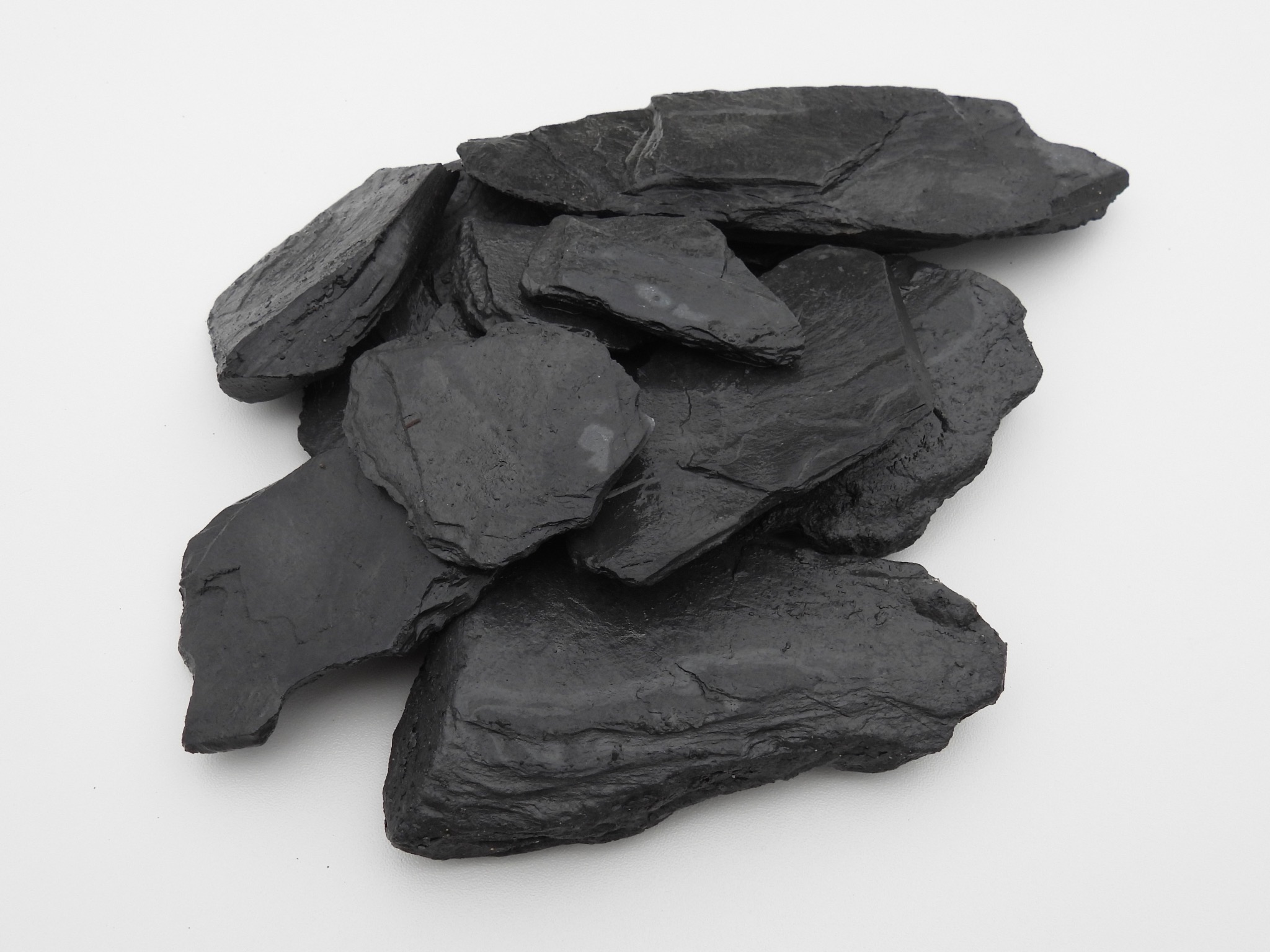 Stos szaro-czarnych, nieregularnych kamieni łupkowych na białym tle, prezentacja materiału.