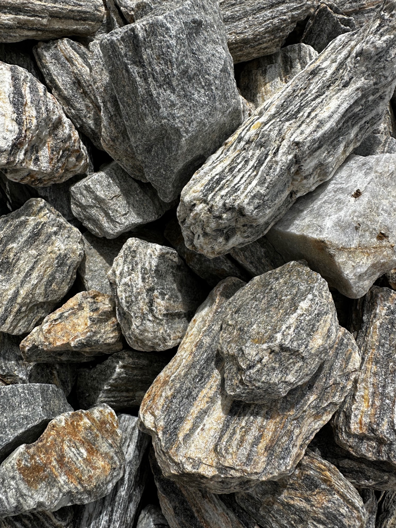 Stos szaro-białych kamieni granitowych o wyraźnych, ciemnych smugach, niektóre z rdzawymi przebarwieniami, ułożonych blisko siebie.