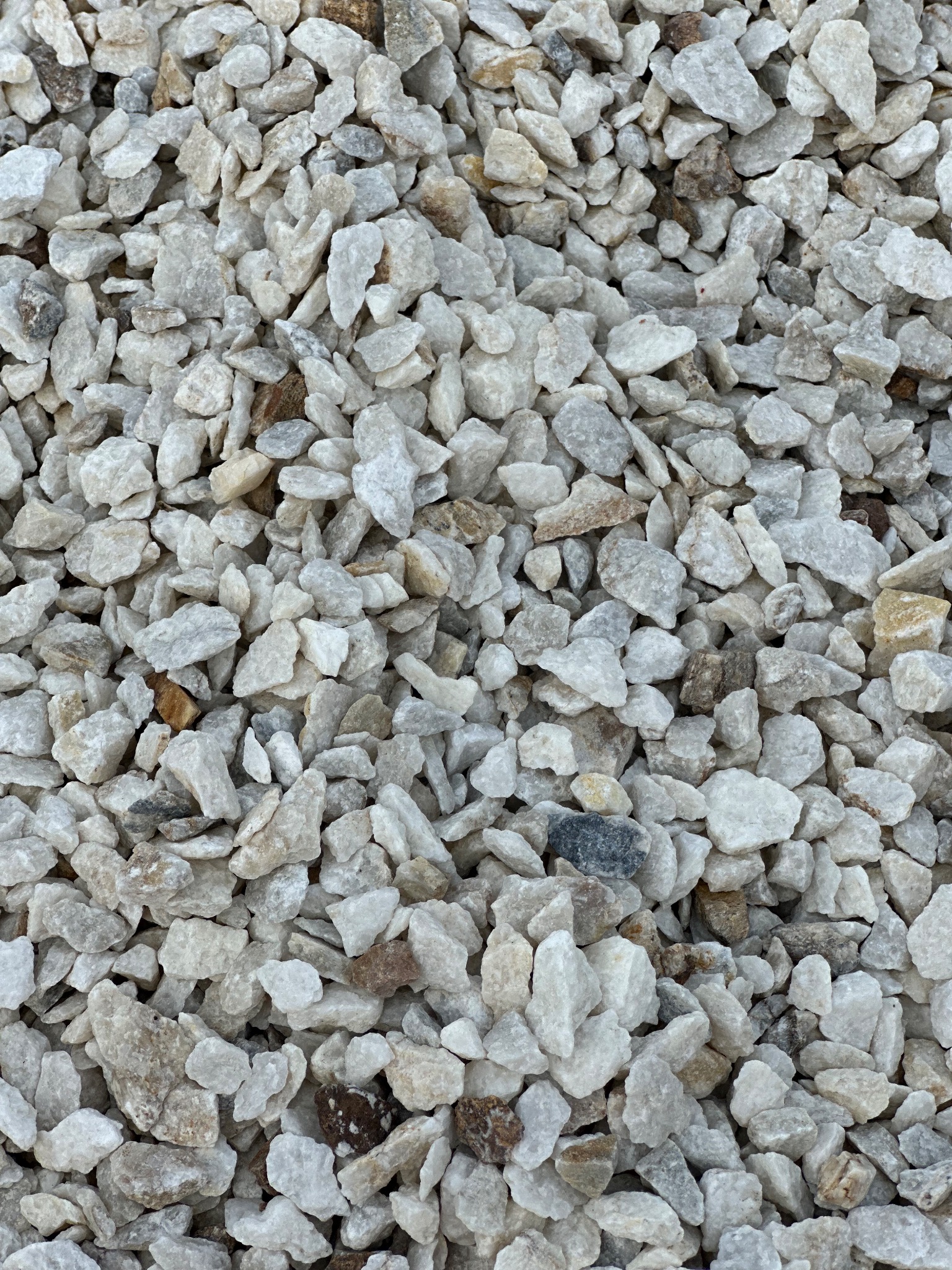 Biały grys marmurowy o nieregularnych kształtach i zróżnicowanej fakturze, z widocznymi drobnymi brązowymi i szarymi elementami.