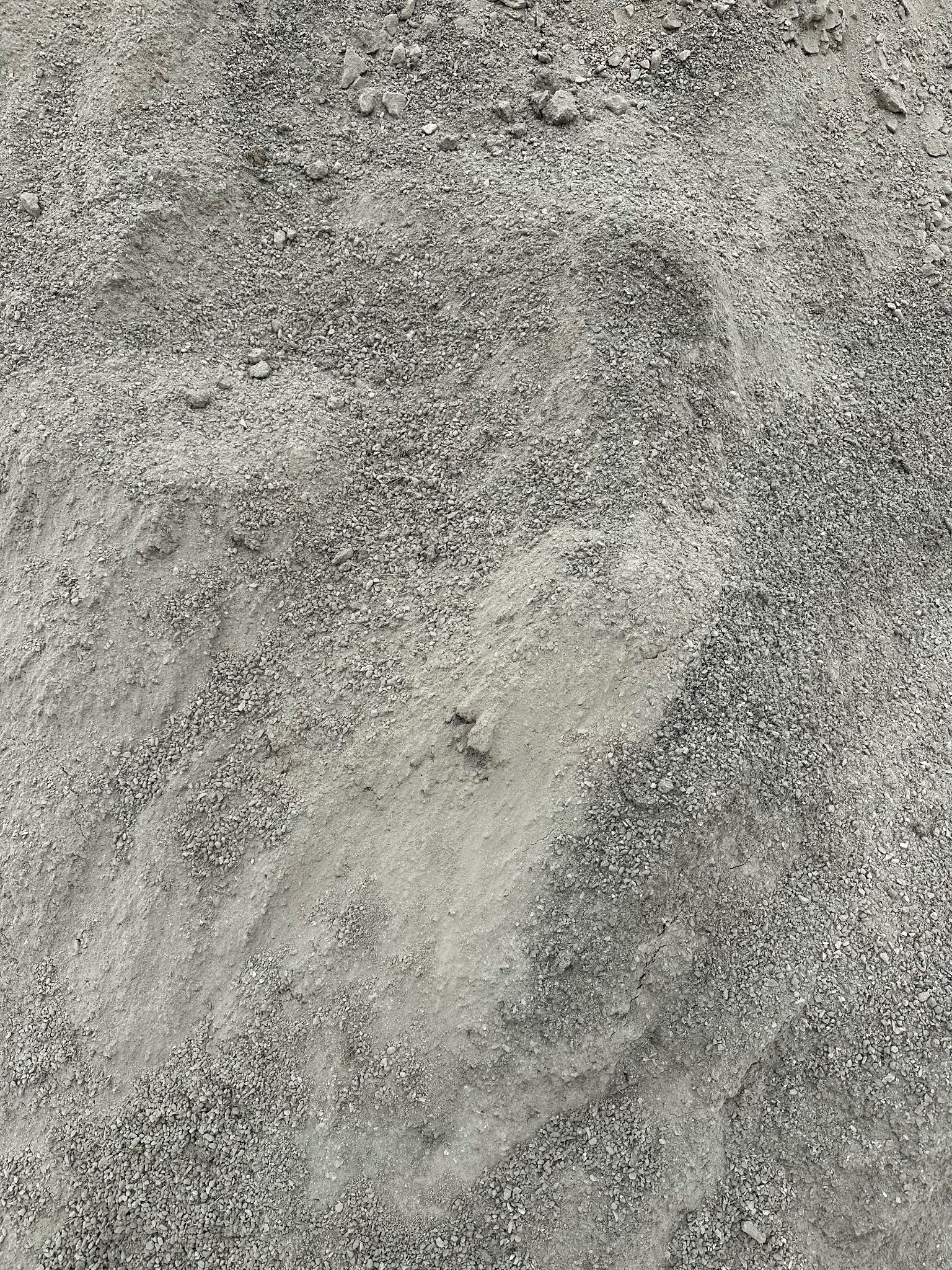 Góra szarego żwiru o zróżnicowanej granulacji, z widocznymi śladami po przesunięciu materiału.