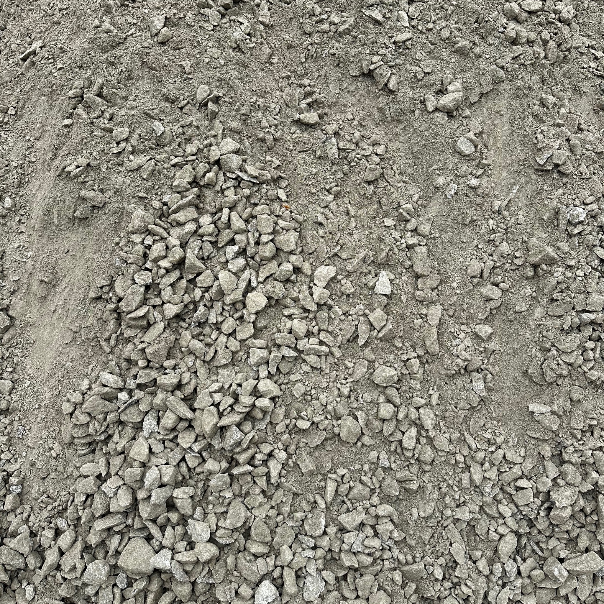 Kruszywo o frakcji mieszanej, składające się z drobnego piasku i większych, szarych kamieni, tworzące nieregularną powierzchnię z wyraźnymi śladami po transporcie lub przesypywaniu.
