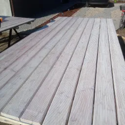 Deski tarasowe z ryflowaną powierzchnią ułożone na konstrukcji, widok z góry, w tle dom jednorodzinny i zaparkowany samochód osobowy.