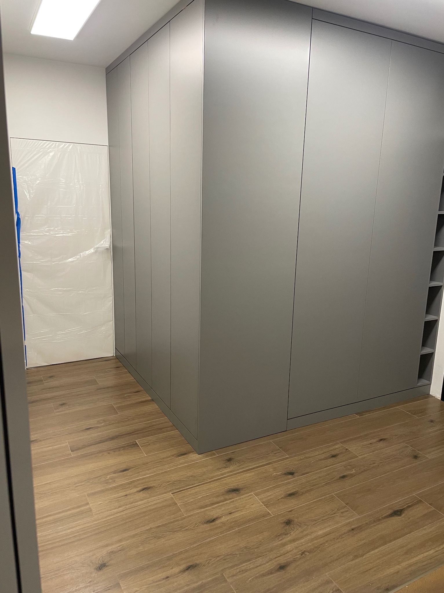 Szara szafa wnękowa z półkami, wykonana na wymiar, z drewnopodobną podłogą, drzwi zabezpieczone folią ochronną.