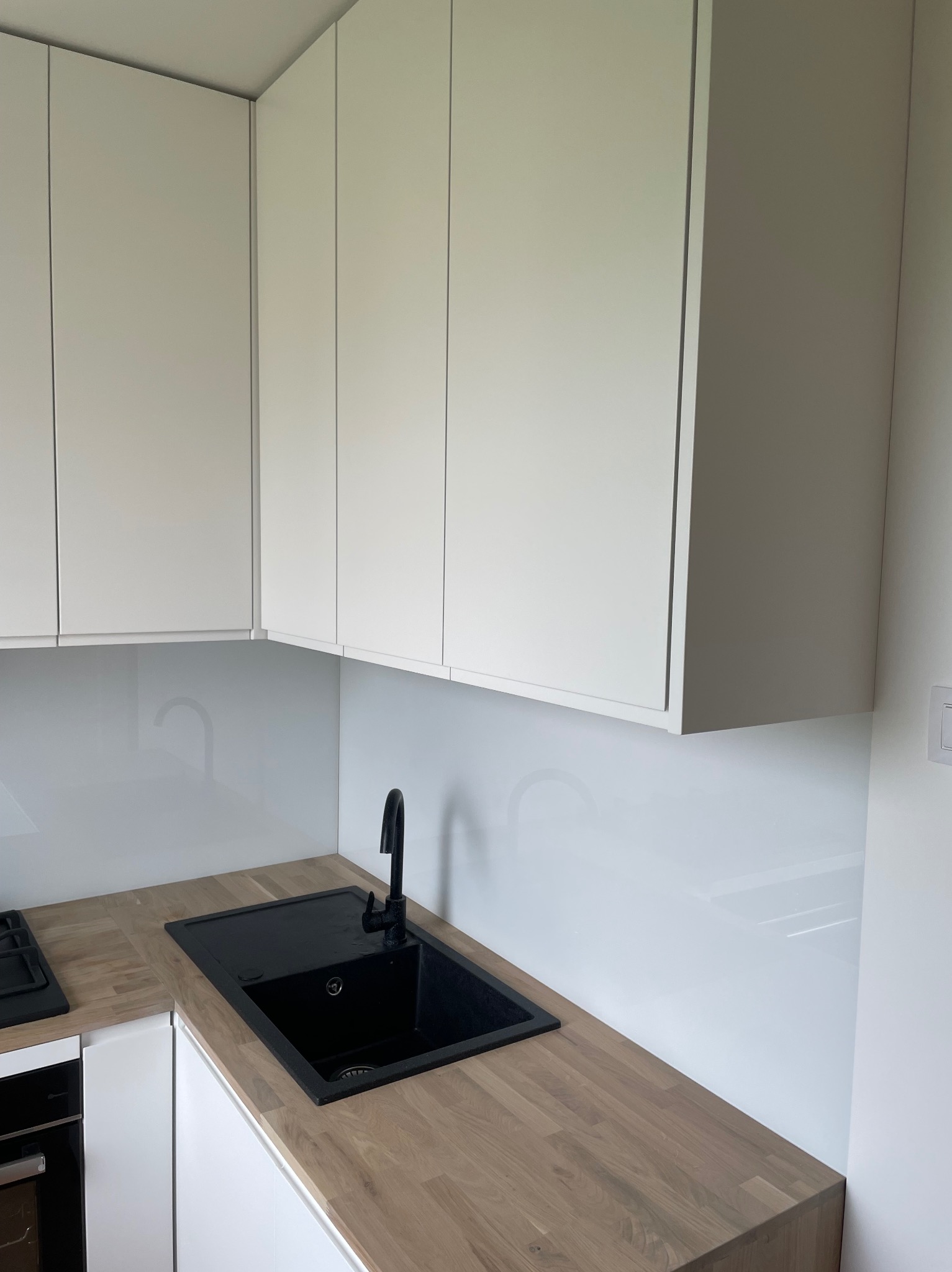 Nowoczesna kuchnia z białymi szafkami, drewnianym blatem i czarnym zlewem granitowym z baterią, minimalistyczny design, jasne wnętrze.