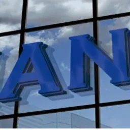 Niebieski napis 'FINANCE' na szklanej fasadzie budynku biurowego, odbijający błękitne niebo z chmurami.