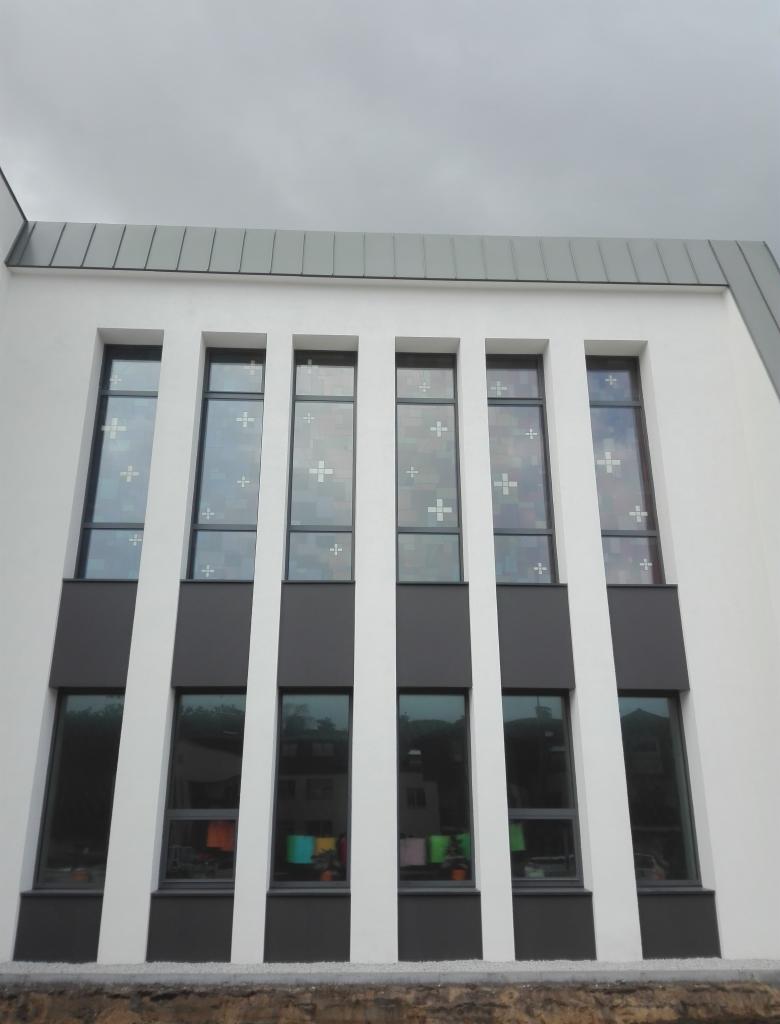 Fasada budynku z rzędem wysokich, wąskich okien z krzyżami w górnej części, osadzonych w białej elewacji z szarymi elementami wykończeniowymi.
