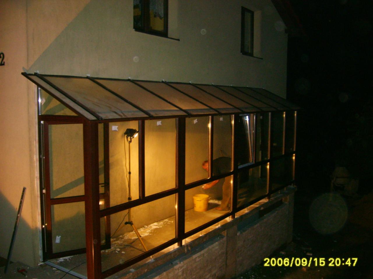 Montaż przeszklonej werandy z ramą PCV przy ścianie budynku, widoczne narzędzia i oświetlenie robocze, data na zdjęciu 2006/09/15.