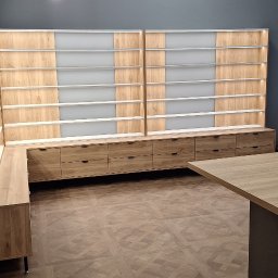 Mateusz Zdanowski - Duża, narożna szafa wnękowa z szufladami i podświetlanymi półkami, w jasnym odcieniu drewna, na podłodze wzór parkietu, widok na ulicę przez okno.