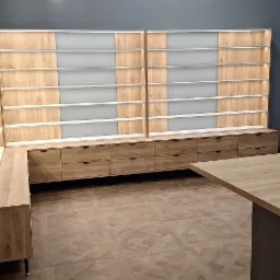 Duża, narożna szafa wnękowa z szufladami i podświetlanymi półkami, w jasnym odcieniu drewna, na podłodze wzór parkietu, widok na ulicę przez okno.