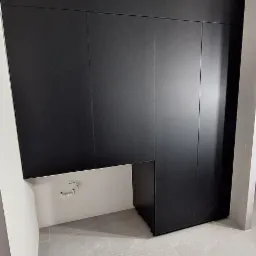 Ciemna zabudowa meblowa na wymiar w nowoczesnym wnętrzu. Minimalistyczny design, gładkie fronty, szara płytka na podłodze. Widoczna instalacja wodna.