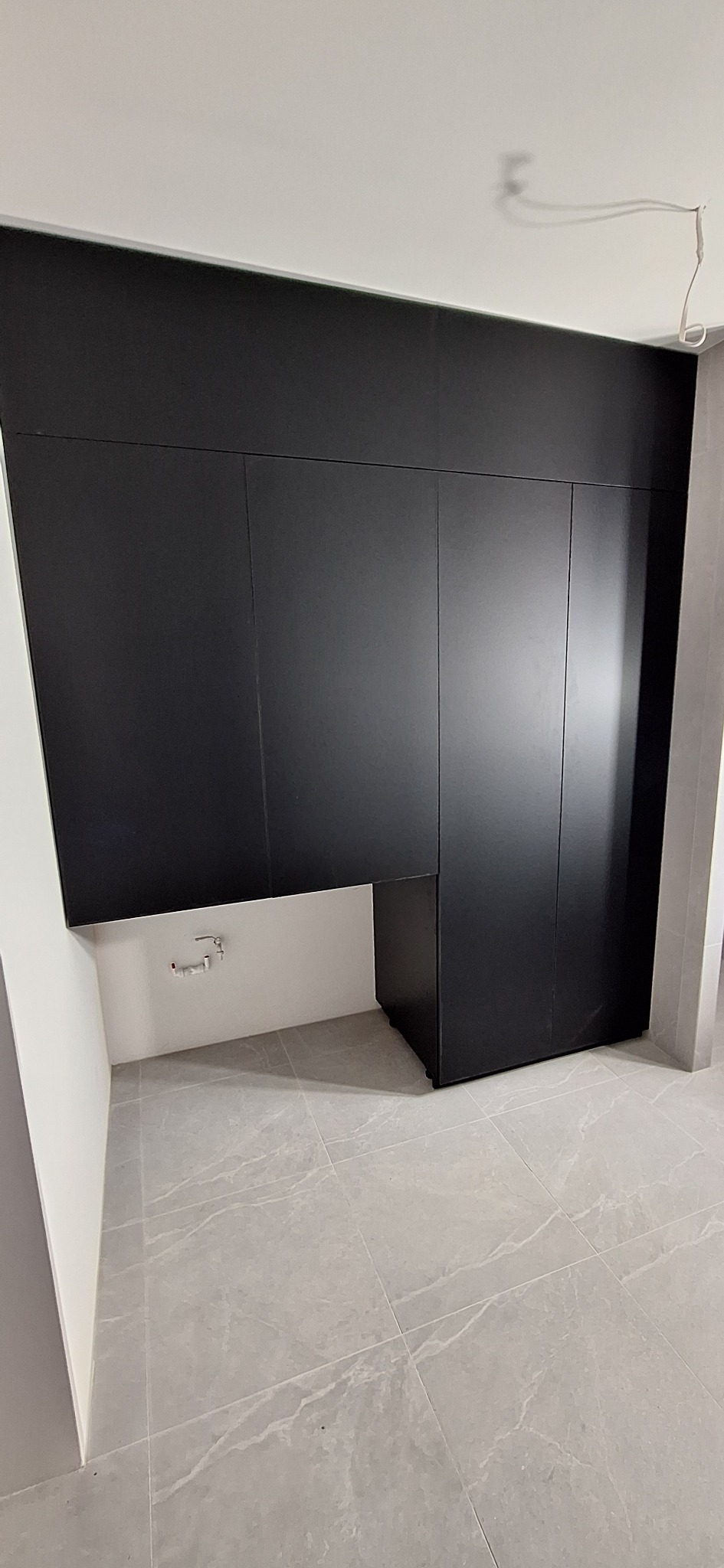 Ciemna zabudowa meblowa na wymiar w nowoczesnym wnętrzu. Minimalistyczny design, gładkie fronty, szara płytka na podłodze. Widoczna instalacja wodna.