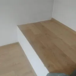 Wykończona wnęka z płyt kartonowo-gipsowych zabudowana panelami podłogowymi imitującymi drewno, białe ściany, widoczne łączenie paneli na krawędzi wnęki.