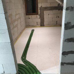 HYDRO-THERM SPÓŁKA Z OGRANICZONĄ ODPOWIEDZIALNOŚCIĄ - Izolacja podłogowa z zielonymi rurami ogrzewania podłogowego w surowym wnętrzu z bloczków. Widoczne okno i fragment poddasza.