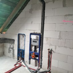 HYDRO-THERM SPÓŁKA Z OGRANICZONĄ ODPOWIEDZIALNOŚCIĄ - Instalacja wodno-kanalizacyjna w surowym wnętrzu: rury w ścianach z betonu komórkowego, stelaż podtynkowy WC Cersanit, widoczne piony i poziomy rur.