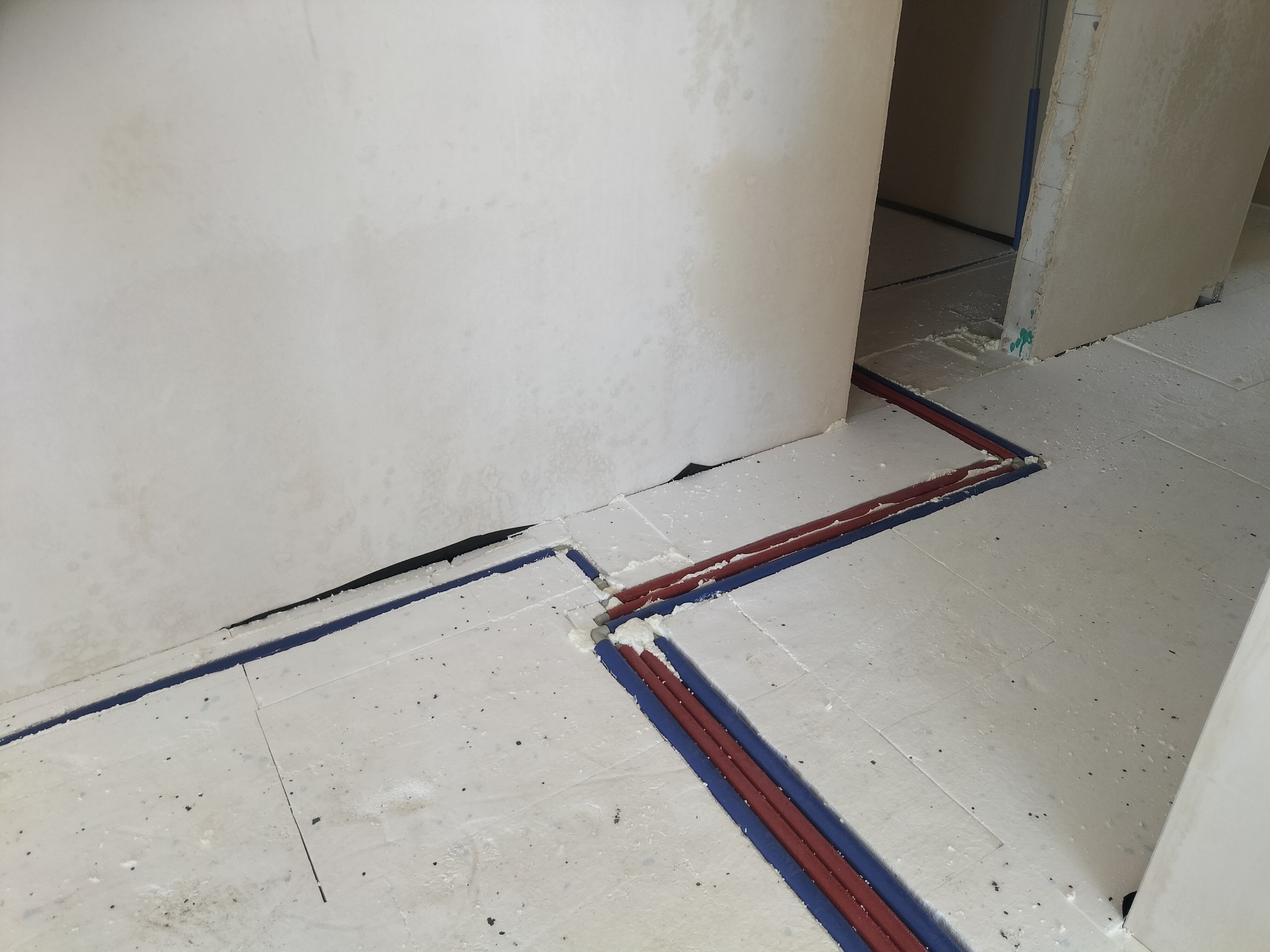 Biała izolacja podłogowa z czerwono-niebieskimi rurami ogrzewania podłogowego, widok z góry, surowy stan wykończenia wnętrza, pianka montażowa w szczelinach.
