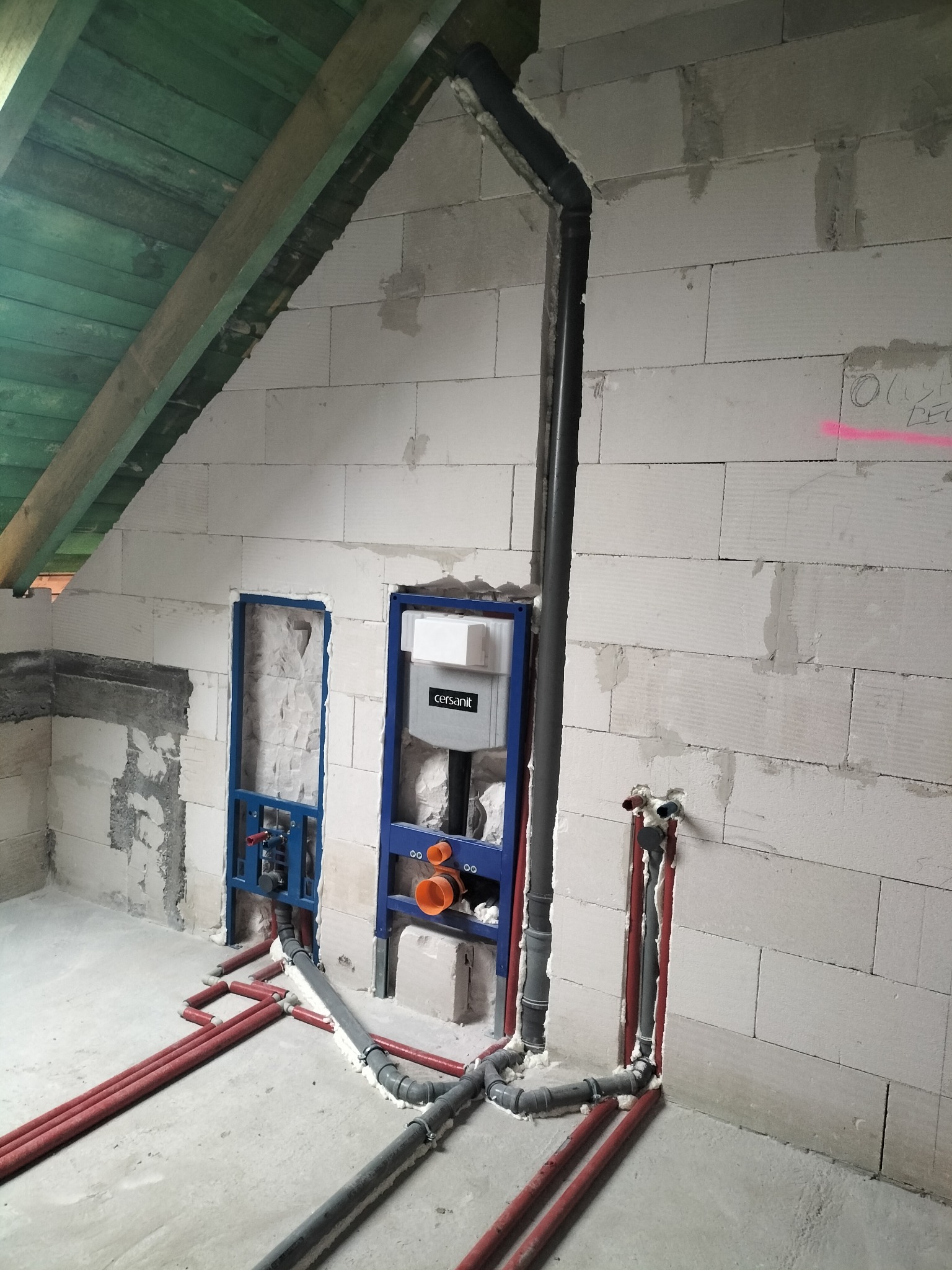 Instalacja wodno-kanalizacyjna w surowym wnętrzu: rury w ścianach z betonu komórkowego, stelaż podtynkowy WC Cersanit, widoczne piony i poziomy rur.
