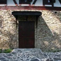 Wejście do budynku z kamienną elewacją i zadaszeniem nad drzwiami, widoczny fragment chodnika z kamiennej kostki