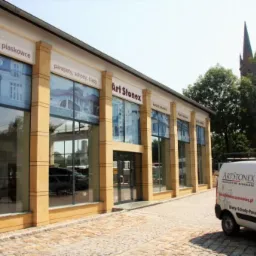 Budynek firmy Art Stonex z dużymi oknami wystawowymi prezentującymi aranżacje z kamienia naturalnego i piaskowca, widoczny firmowy samochód dostawczy z logo i ofertą: blaty, schody, parapety...