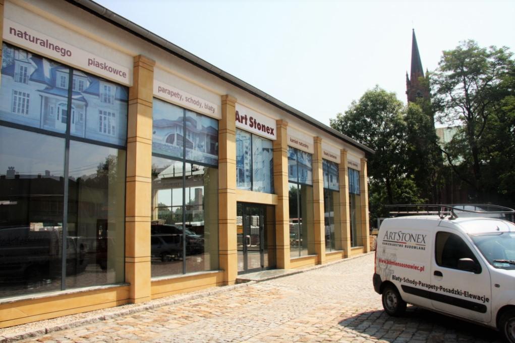 Budynek firmy Art Stonex z dużymi oknami wystawowymi prezentującymi aranżacje z kamienia naturalnego i piaskowca, widoczny firmowy samochód dostawczy z logo i ofertą: blaty, schody, parapety...