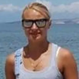 Uśmiechnięta blondynka w dżinsowym kombinezonie i okularach przeciwsłonecznych na tle błękitnego morza i nieba.