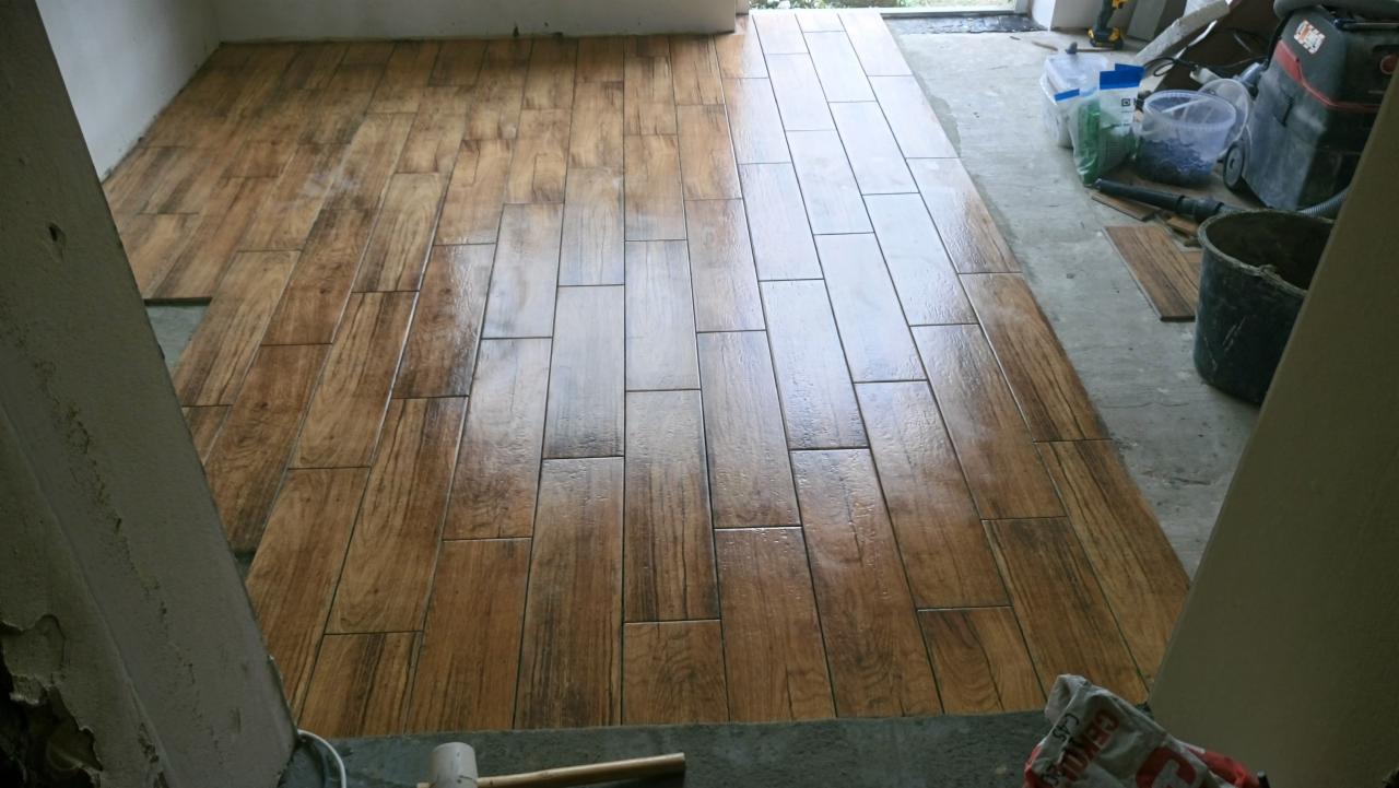 Ułożona podłoga z płytek imitujących drewno, widoczny fragment ściany w trakcie prac wykończeniowych, na obrzeżach narzędzia i materiały budowlane.